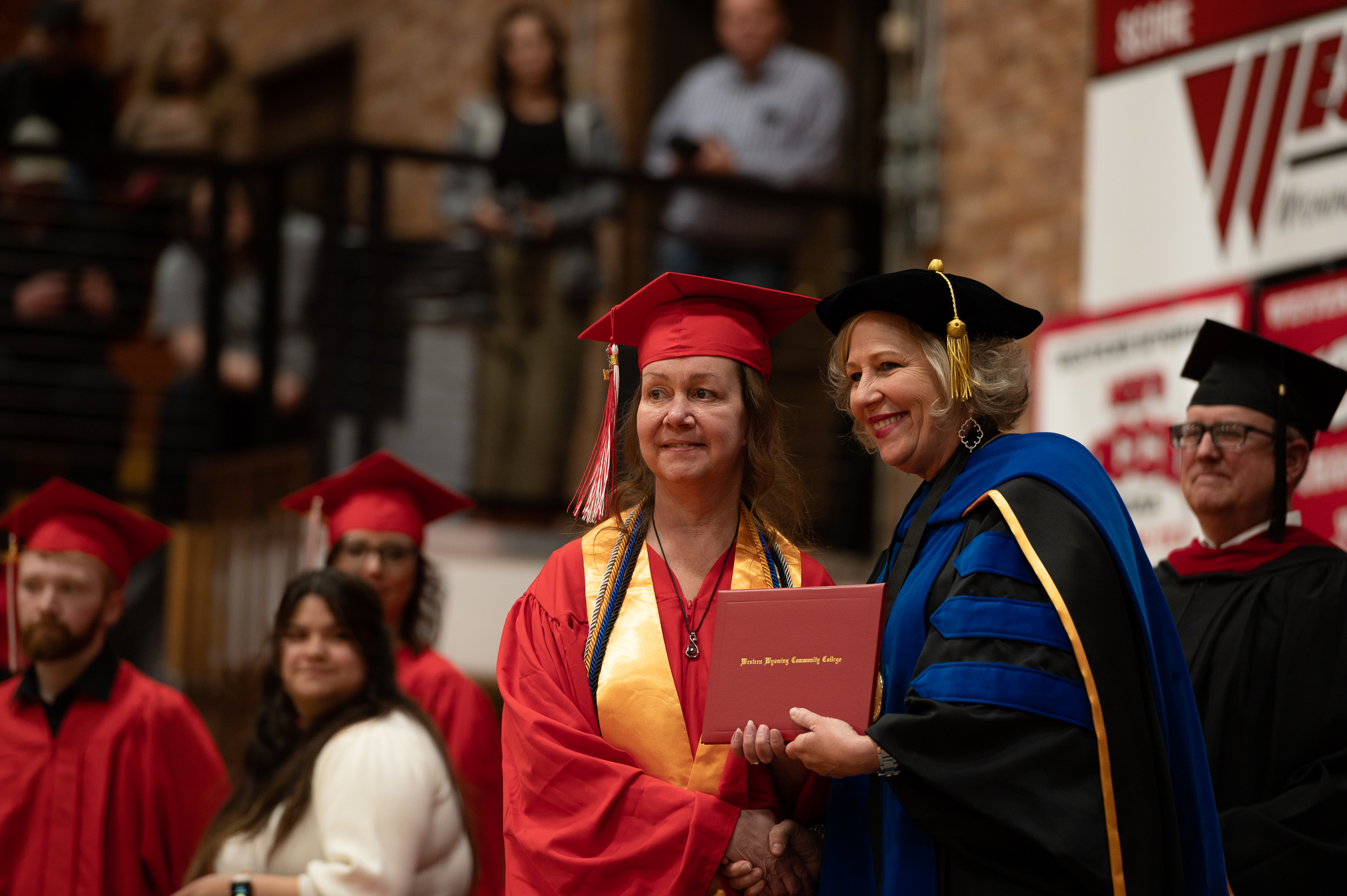 Student posing with college president and receiving diploma 