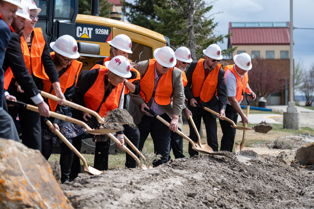 Group photo of Western Board of Trustees, Dr. Kim Dale President, VP Administrative Services Burt Reynolds, Nursing Chair Heidi Brown and Director of Facilities Chris Dever posing with golden shovels in hand digging at the construction site. 