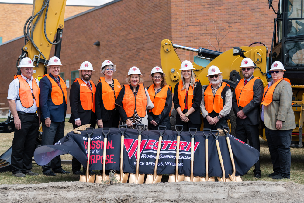 Group photo of Western Board of Trustees, Dr. Kim Dale President, VP Administrative Services Burt Reynolds, Nursing Chair Heidi Brown and Director of Facilities Chris Dever posed in front of golden shovels at the construction site. 