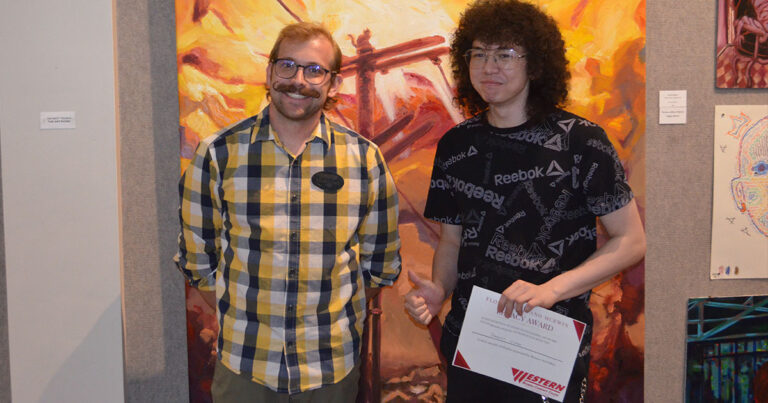 Western Wyoming College Assistant Professor of Art Ben Nathan stands with Jarrett Nipper after Nipper was named the recipient of the Florence Alfano McEwin Legacy Award for his oil on canvas work “This is How I See my Cat.” Professor Nathan and a student proudly display a certificate for the student's art featured on this year's literary journal cover. Large painting in red and orange is hung on the wall behind them.