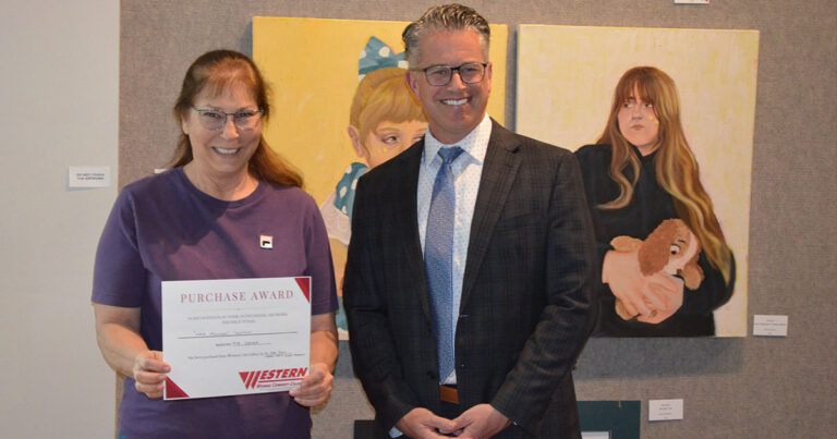 Dr. Young and Rita Osborne stand together, holding a certificate, with artistic paintings displayed in the background.