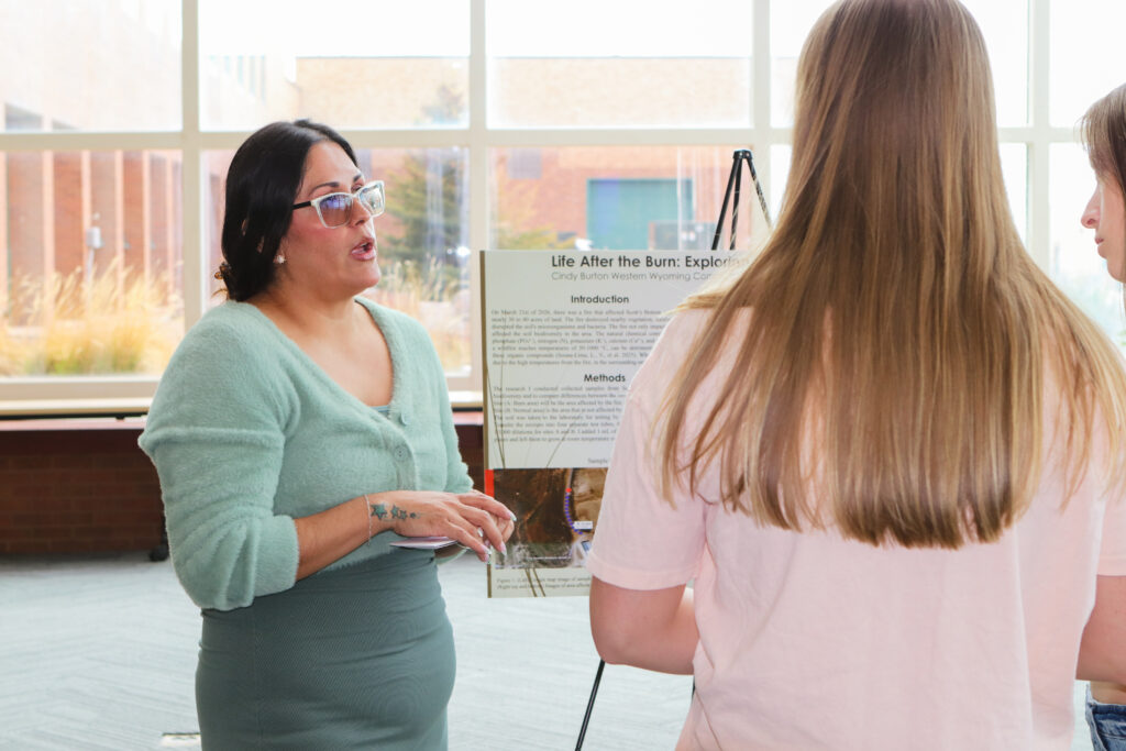 3. A woman converses with two girls, standing in front of a large educational poster.