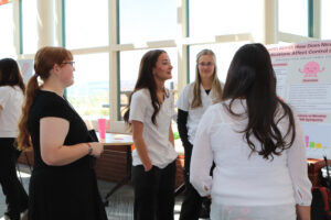 Several individuals stand together, engaged in conversation while examining a poster displayed nearby.