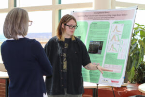 A student and another woman stand next to a poster board, engaged in discussion or presentation.