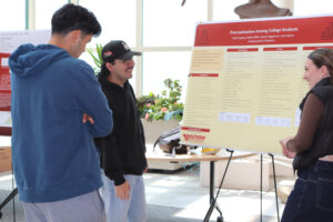 Three individuals observing a poster on a stand, engaged in discussion