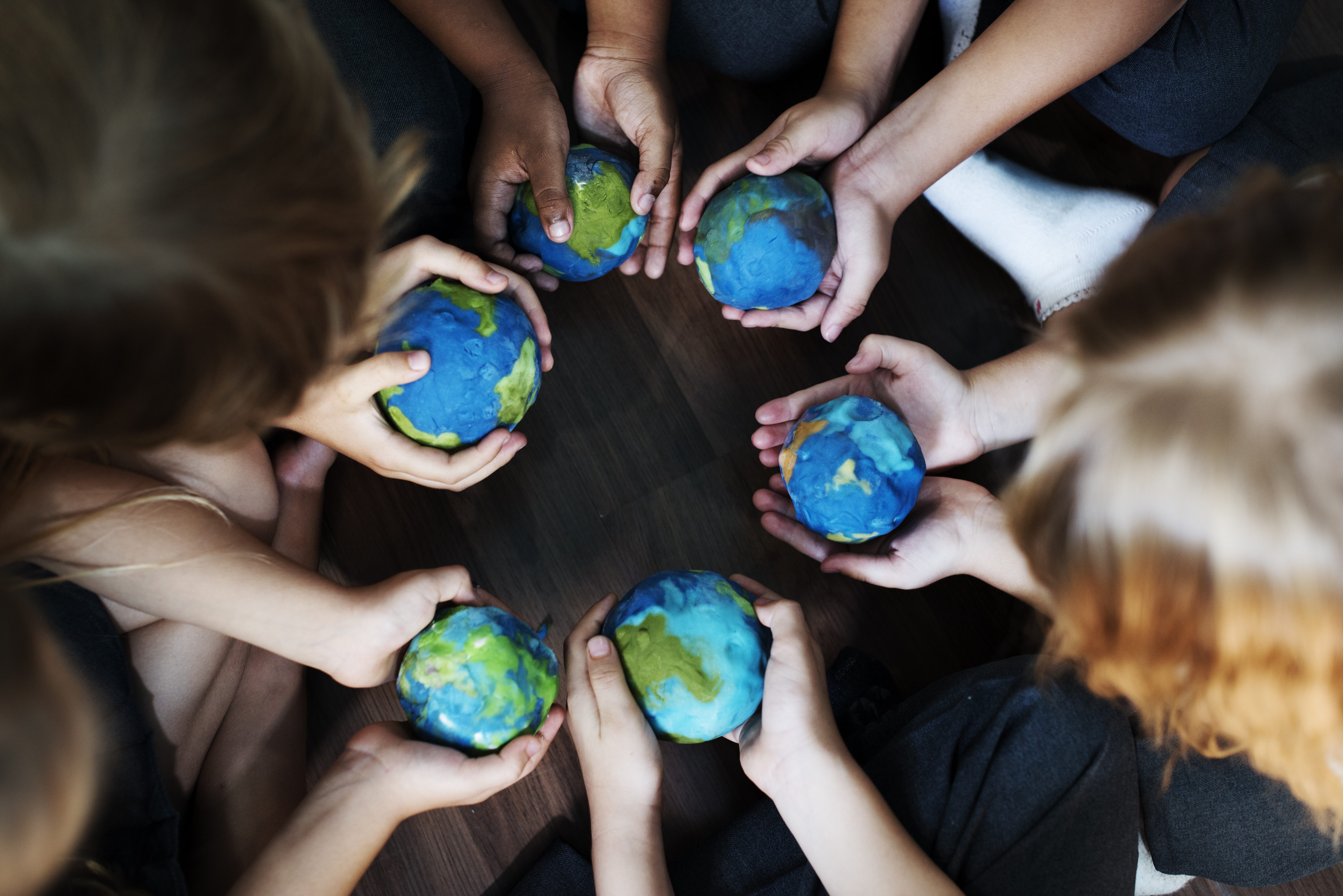 Group of diverse kids' hands holding globes in a circle