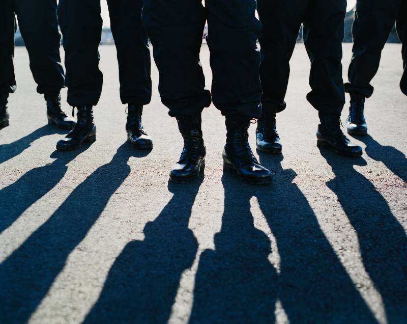 Low photo of black pant clad legs in shiny black boots on pavement
