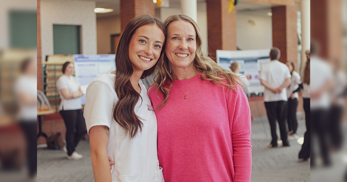 Two women, Madison Yoak and Carla Lee, stand side by side in a hallway, representing student and professor roles.