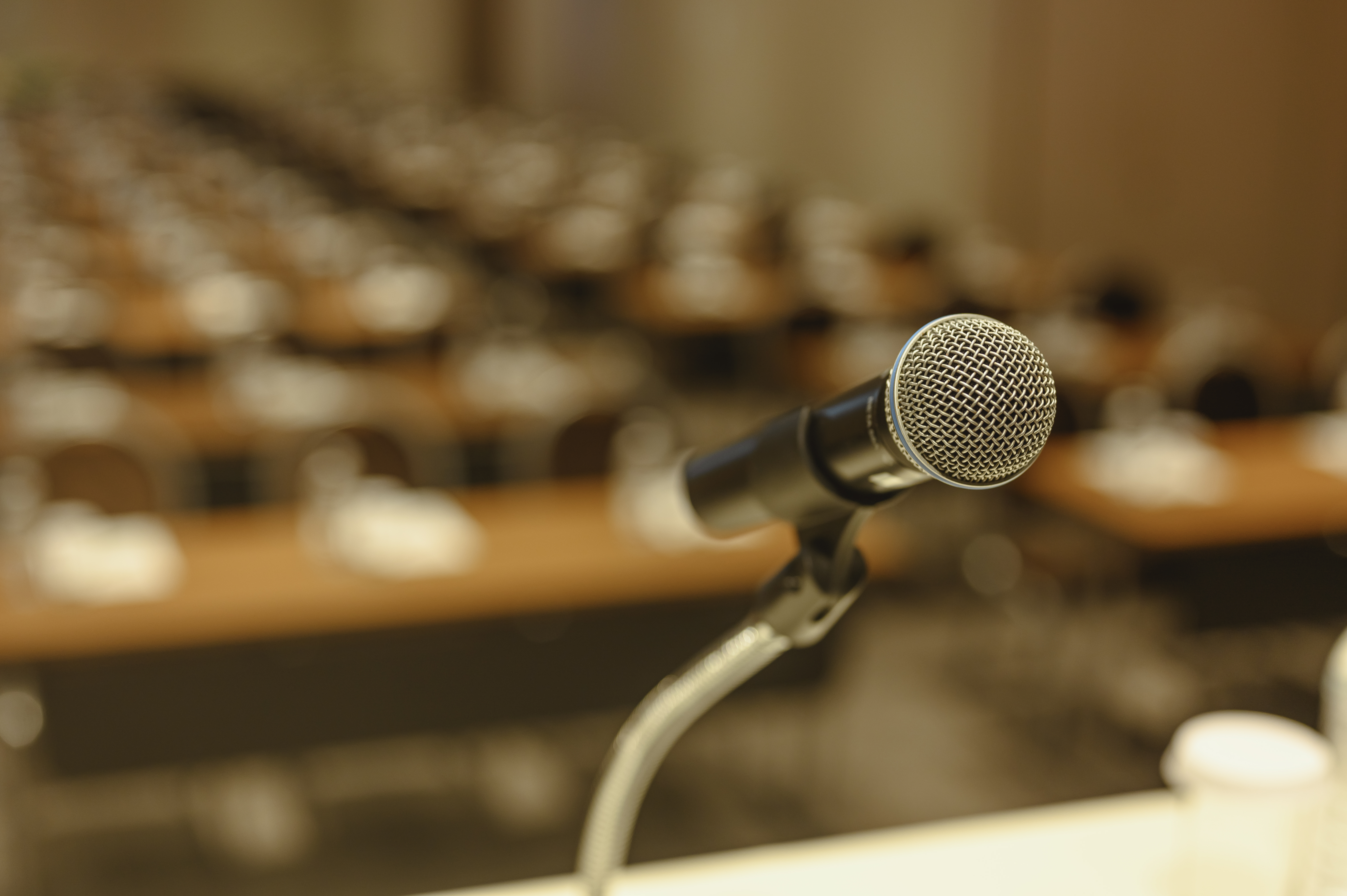 close-up photo of a microphone against a blurred background of a conference room or lecture hall