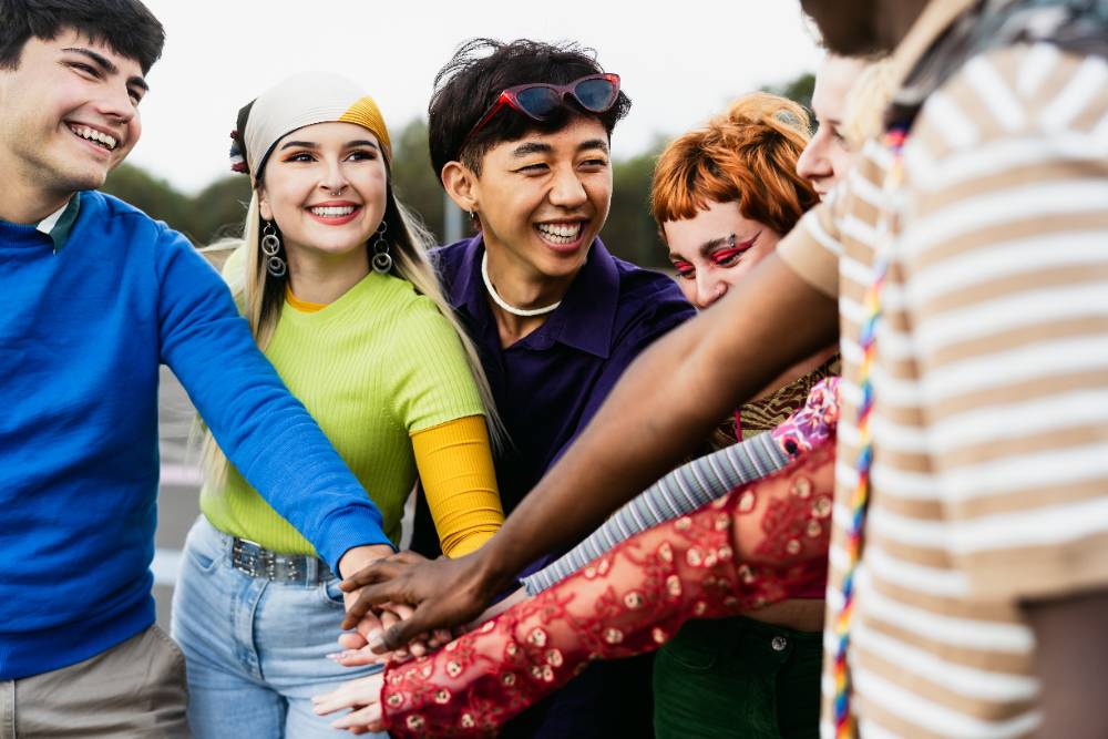 Happy young diverse friends having fun stacking hands together outdoor