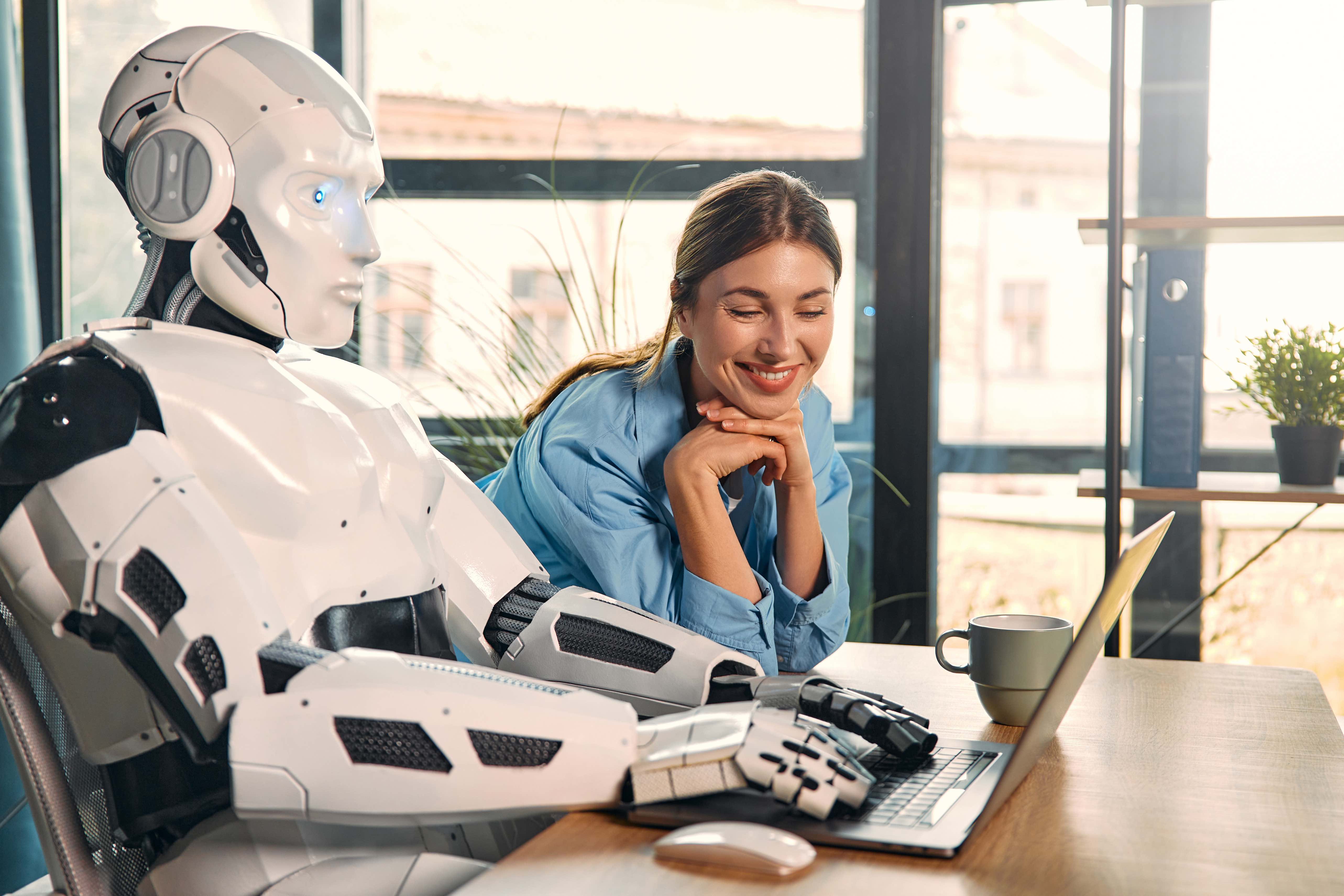 A women sitting with a robot at a computer. 