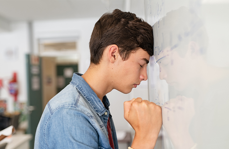Student leaning on whiteboard looking frustrated. 