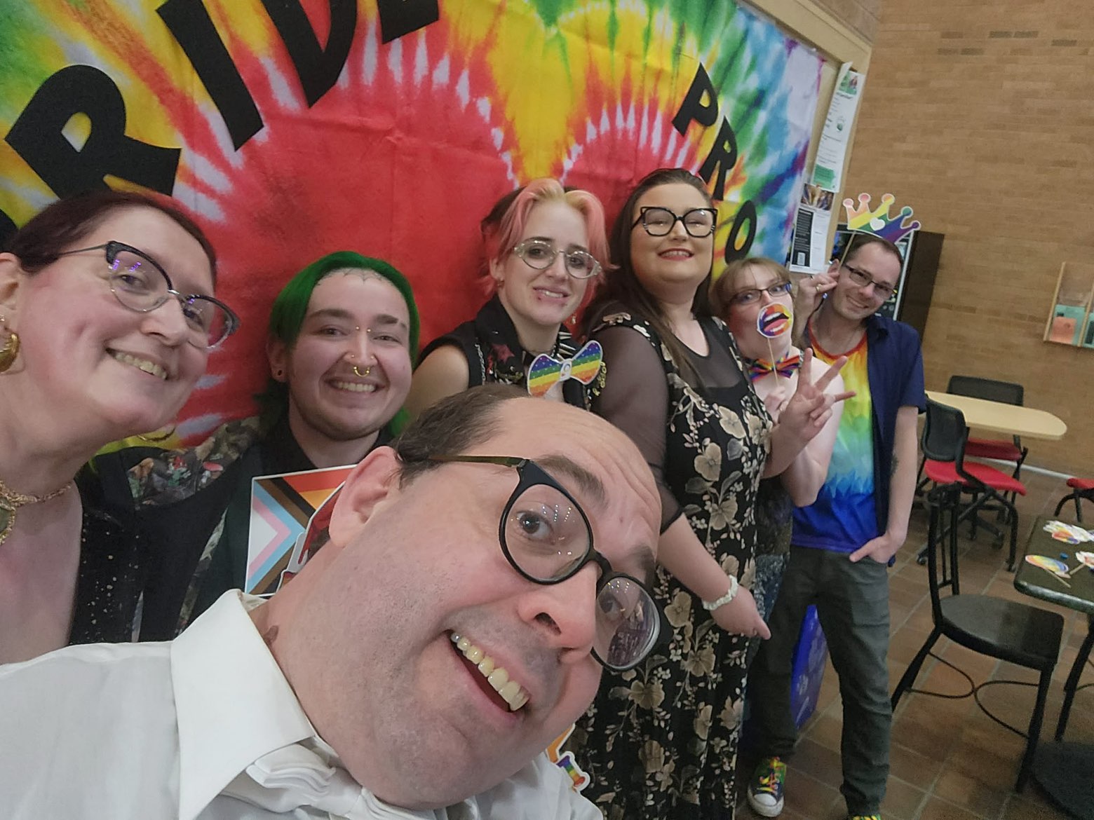 A group of smiling people pose in front of a vibrant, rainbow tie-dye banner with 